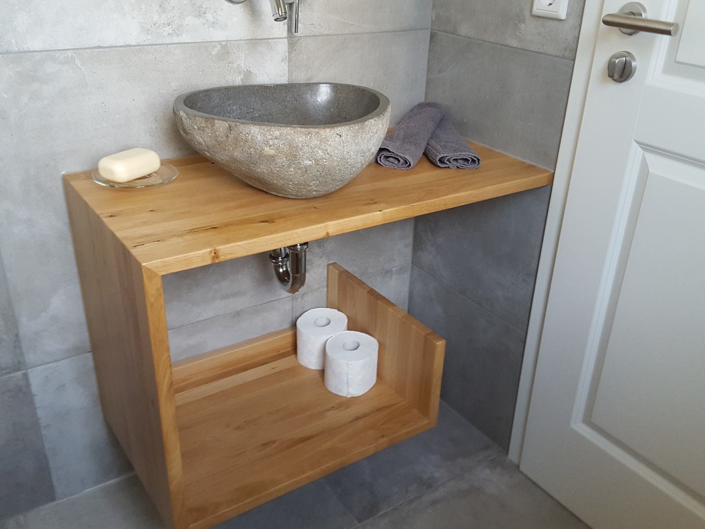 Waschtisch mit steinernem Waschbecken und Regalablage darunter. 